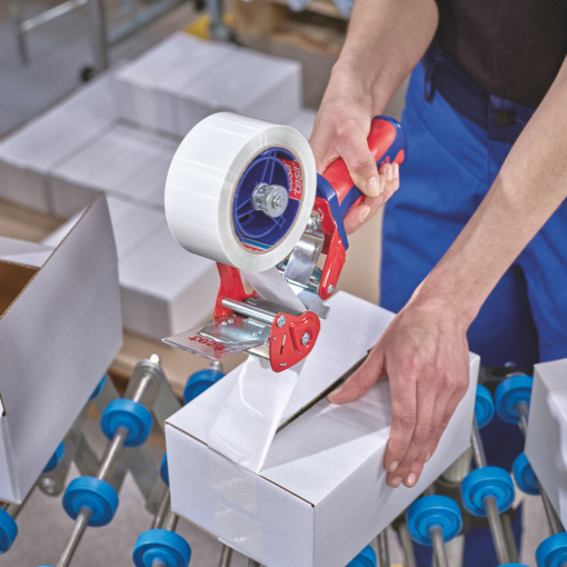 Pracownik zakleja biały karton przezroczystą taśmą tesa® z użyciem ręcznego dyspensera.