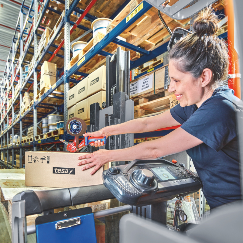 Pracowniczka magazynu używa brązowej taśmy tesa® do zaklejania kartonu na palecie.