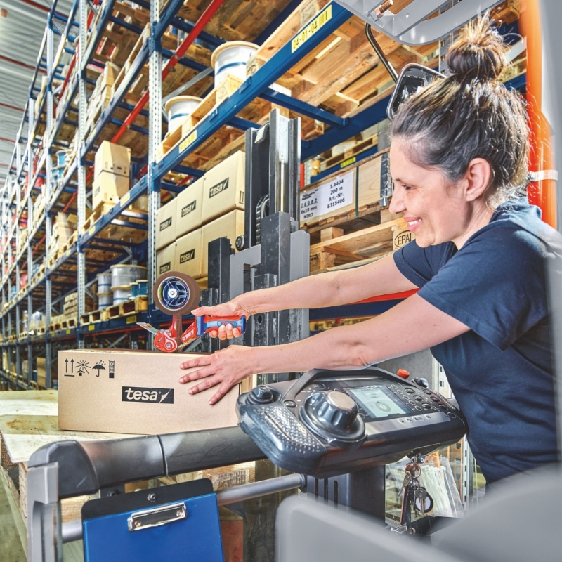 Pracowniczka magazynu używa brązowej taśmy tesa® do zaklejania kartonu na palecie.