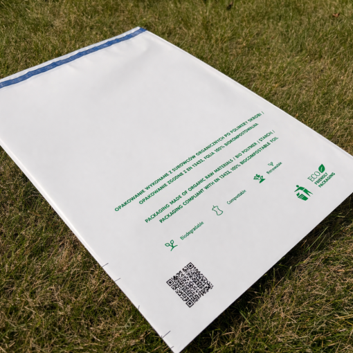 Biały foliopak biodegradowalny leżący na trawie, widoczny kod QR i informacja o kompostowalności